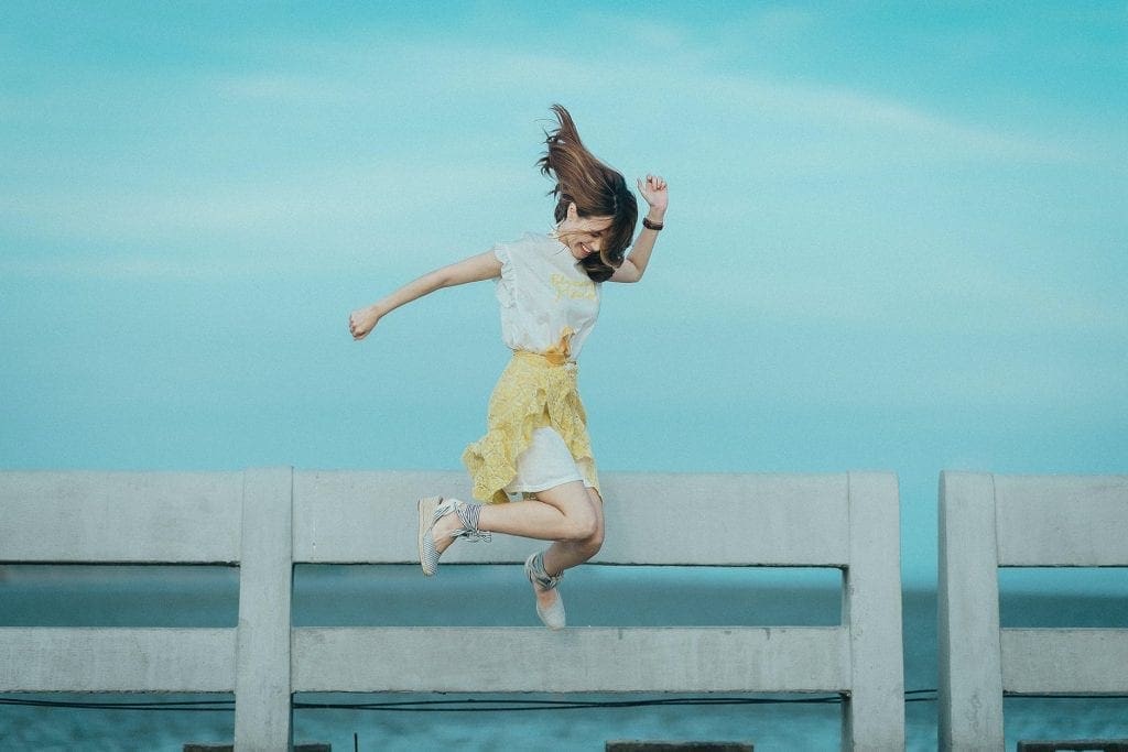 jumpshot photography of woman in white and yellow dress near body of water symbolising taking action